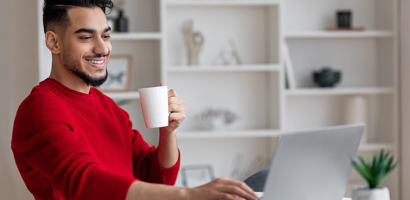 Happy man drinking coffee whilst on laptop